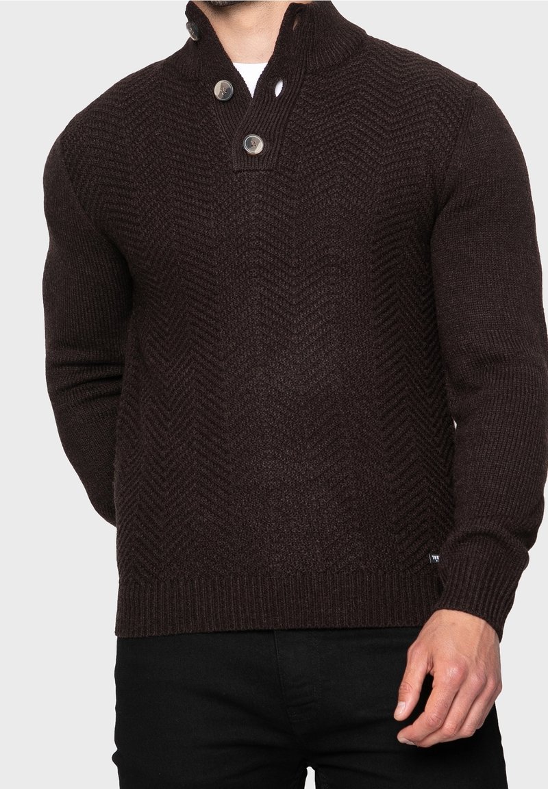 Maglione lavorato a maglia marrone scuro con un motivo a spina di pesce testurizzato, colletto alto e due bottoni decorativi all'collo.