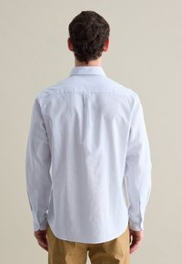Camisa de botones a rayas azul claro con un cuello estrecho, mangas largas y un dobladillo redondeado. Presenta acentos de botones blancos en los puños.
