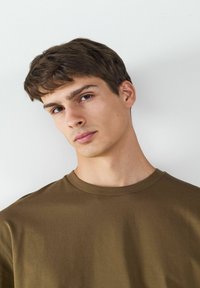 Brown cotton t-shirt with a crew neck, smooth texture, and short sleeves, displayed on a male model against a neutral background.