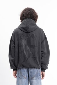 Felpa nera oversize con un design grafico testurizzato e luccicante sulla schiena. Tessuto morbido, polsini e orlo a costine, con cappuccio regolabile tramite coulisse.