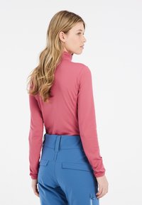 Top a maniche lunghe di rosa pallido, con colletto a imbuto. Abbinato a pantaloni a vita alta blu chiaro, con tasche e una texture liscia.