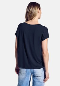 Haut noir à manches courtes avec une coupe décontractée, un col rond et une texture lisse, associé à un jean bleu clair dans un style décontracté.