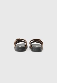 Brune lædersandaler med sorte gummisåler, der har justerbare stropper og et tekstureret design. Åben tå stil med minimalistisk design.