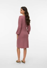 Abito lavorato a maglia in rosa chiaro con maniche lunghe a palloncino e texture a coste, che arriva fino a metà polpaccio. Design semplice e aderente senza decorazioni.