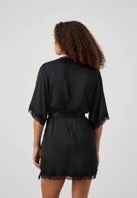 Robe en satin noir à manches courtes, avec des bordures en dentelle aux poignets et à l'ourlet, et une taille à nouer. Texture lisse et design à mi-cuisses.