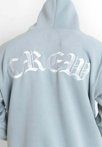 Felpa leggera blu chiaro con grande scritta ricamata "CREW" in bianco. Il design prevede un cappuccio e un tessuto morbido e strutturato.