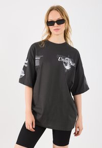 T-shirt oversized preto com estampas gráficas em branco, apresentando um design de lua e detalhes em texto. Acompanhado de calções de bicicleta pretos.