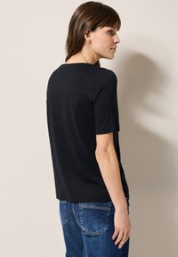T-shirt noir à manches courtes en tissu doux, avec un col rond et une coupe décontractée. Le dos présente un subtil détail de couture horizontale.