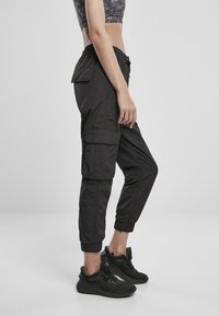 Zwarte cargobroek met een slim fit, elastische boorden en zijzakken. Gemaakt van lichtgewicht materiaal met een gladde textuur. Gecombineerd met zwarte sneakers.