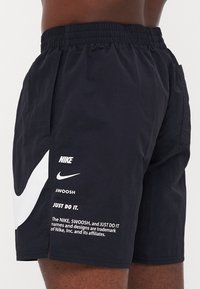 Pantaloni sportivi neri con vita elasticizzata. Presentano un grande logo Nike swoosh bianco e testo stampato sul lato. Tessuto leggero.