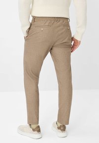 Beige tapered trousers van een gestructureerde stof met twee achterzakken, voorzien van gestikte details en een middelhoge taille. Gekocht met witte sneakers.