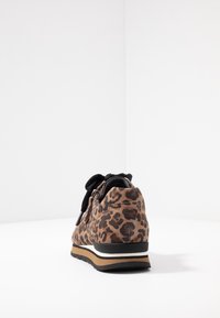 Brązowy sneaker w cętki lamparta z czarną elastyczną sznurowadłem, materiałową cholewką i kontrastową gumową podeszwą. Posiada zamek błyskawiczny i teksturowane akcenty.