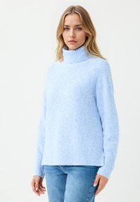Helleblaue Sweater mit einem gerippten Rollkragen, weichem Material und langen Ärmeln. Bietet eine lässige Passform und ein dezentes Muster. Kombiniert mit blauen Jeans.