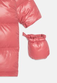 Rosa Pufferjacke mit glänzender, gesteppten Textur und übergroßen Ärmeln. Begleitet von einem passenden, gerafften Beutel.