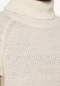 Light beige turtleneck sweater made of textured knit fabric, featuring a loose fit and ribbed collar for comfort and style.