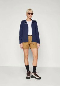 Ναυτικό ελαφρύ μπουφάν με κουκούλα, λευκό μπλουζάκι, καφέ σορτς, μαύρες κάλτσες και μπότες πεζοπορίας. Το μπουφάν διαθέτει μπροστινό φερμουάρ και λεπτομέρεια με λογότυπο.