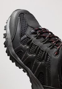 Black athletic shoe featuring a mesh upper for breathability, textured synthetic accents, and a rugged rubber sole with grip-enhancing tread.