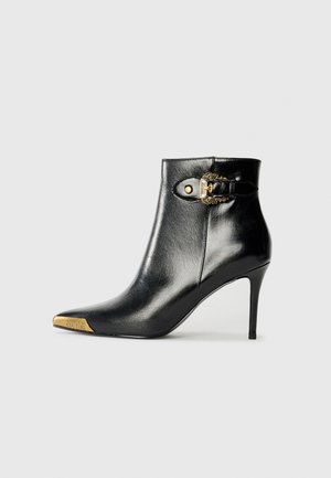 Sorte skinn ankelstøvler med spiss tå og stiletthæl. Har en gullakk accent på tåpartiet og en detaljer med spenne på siden.