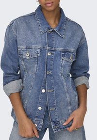 Chaqueta de mezclilla en azul claro con un corte clásico, que cuenta con dos bolsillos en el pecho, botones plateados y mangas arremangadas.
