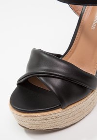 Sandale compensée en cuir noir à bouts ouverts avec des brides croisées et une semelle plateforme en jute tressé.