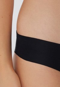 Matériau en bande extensible noire, texture lisse, formant un bord sans couture à la taille. Design minimaliste, vue rapprochée de la peau et du tissu.