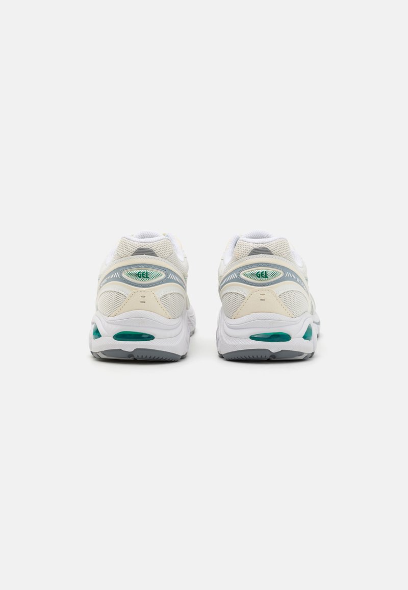 Weiße Sportschuhe mit Obermaterial aus Mesh und Synthetik, mit grünen Akzenten und Gel-Dämpfung. Abgerundete Ferse und strukturiertes Profil für besseren Halt.
