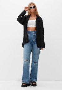 Must valge oversize nööpidega särk, valge lühikeste varrukatega topp, laienevad kulunud heledad teksad, jämedad mustad sandaalid, valged prillid.