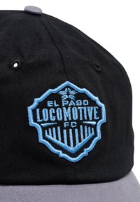 Sort og grå cap med blåt broderet El Paso Locomotive FC-logo med et stiliseret vinget emblem og lodrette striber.