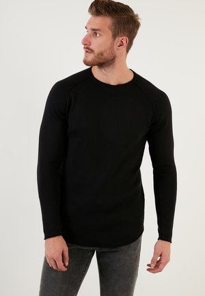Zwarte geribbelde lange mouw shirt met een ronde halslijn en raglanmouwen, voorzien van een licht gebogen zoom en een zachte textuur.