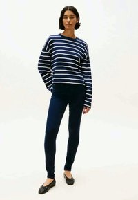 Sweater riscado em azul marinho e branco com decote redondo, combinado com calças escuras e sapatilhas pretas. Tecido liso, ajuste confortável, estilo casual.