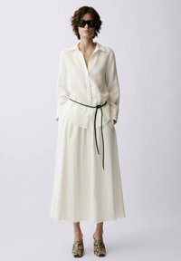 Ensemble chemise et jupe en lin blanc, avec une ceinture noire. Accessoirisé avec des lunettes de soleil noires et des chaussures à imprimé animal. Texture lisse, design fluide.