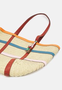 Torebka tote z plecionego słomkowego materiału z pomarańczowymi, niebieskimi, różowymi i czerwonymi skórzanymi akcentami; ma podwójne czerwone skórzane uchwyty i dekoracyjne frędzle.