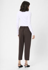 Braune, tapered Hosen mit einem elastischen Bund und seitlichen Taschen, kombiniert mit einem eng anliegenden weißen Langarmshirt und schwarzen Schuhe mit Absatz.