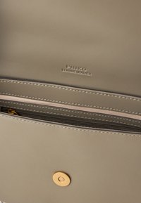 Beige taška z pravé kůže s vnitřním prostorem obsahujícím zipovou kapsu a zlaté patentní uzávěr. Prošité okraje s vyraženým logem značky.