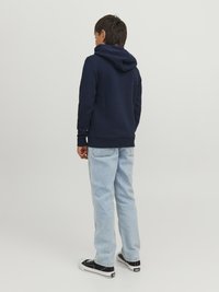 Felpa con cappuccio blu navy dalla texture morbida, abbinata a jeans di jeans chiari. Sneakers bianche e nere completano il look.