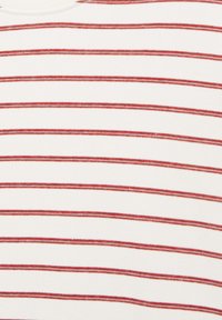 Gros plan d’un tissu blanc avec des fines rayures horizontales rouges espacées de manière régulière.