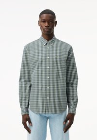 Camisa de cuadros en verde y azul marino, con botones, de mangas largas y cuello, que presenta un pequeño logo en el pecho y botones blancos.