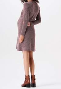 Schwangerschafts kleid im rosa und weißen Fischgrätenmuster, mit langen Ärmeln, knielang, weiche Textur. Kombiniert mit braunen Ankle Boots.