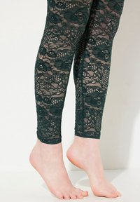 Groene kantleggings met bloemmotieven; semi-doorzacht stof, nauwsluitend tot aan de enkel, afgewerkt met een stevige elastische tailleband.