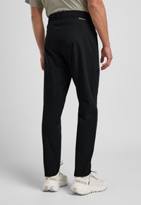 Zwarte sportieve broek met een getailleerd ontwerp en textuurstof, voorzien van een zak en een elastische tailleband, gecombineerd met lichtgekleurde sneakers.