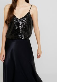 Schwarzes, glitzerndes Tanktop mit dünnen Trägern, kombiniert mit einem schwarzen Satinrock. Das Oberteil hat eine lockere Passform und ein tiefes V-Ausschnittdesign.