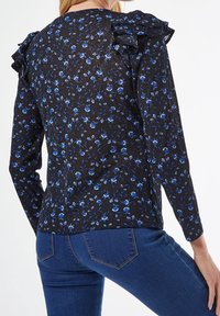 Schwarze Bluse mit langen Ärmeln, die mit blauen Blumenmustern bedeckt ist, mit Rüschen-Schulterdetails und einer leichten Textur.