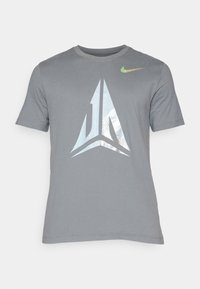 Camiseta gris de manga corta con un gran diseño gráfico reflectante en el centro y un pequeño logo de Nike colorido en la parte superior derecha.