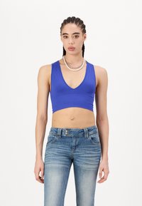 Blå ribbet crop top med V-hals, paret med lyse denimjeans med en falmet design og klassisk lukking med tre knapper.