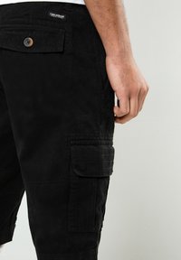 Schwarze Cargo-Shorts aus strapazierfähigem Material, mit einer Seitentasche, Knopfverschluss und Stickdetails. Geeignet für Freizeitkleidung.