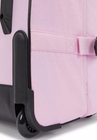 Růžový kufr z látky s černými akcenty, vybavený bočním popruhem, dvojitými kolečky a hladkým povrchem. Kompaktní, obdélníkový design pro cestování.