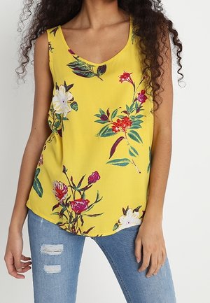 Floral sleeveless top in bright yellow, featuring a scoop neckline and various colorful flower patterns. Paired with light blue ripped jeans.