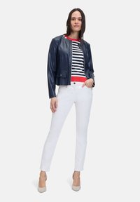 Navy-farbene Kunstlederjacke, gestreiftes Oberteil mit roten Akzenten, weiße Jeans und beige High Heels. Slim Fit, cropped Stil, minimalistische Hardware-Details.