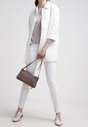 Biały płaszcz na guziki nałożony na szary sweter, w połączeniu z białymi dopasowanymi jeansami i jasnoszarymi butami. Przez ciało przewieszona jest mała brązowa torebka na ramię.