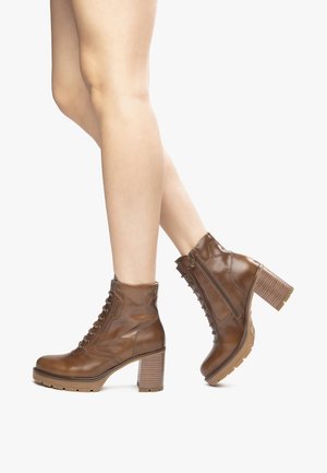 Bottes chevilles en cuir marron avec un talon épais, dotées d'un laçage à l'avant, d'une fermeture éclair sur le côté et d'une semelle en caoutchouc texturée pour une meilleure adhérence.